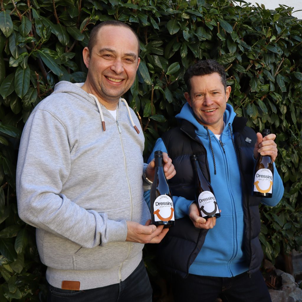 Tim und Steven stehen vor einer Hecke und präsentieren ihre leckeren Salatdressings